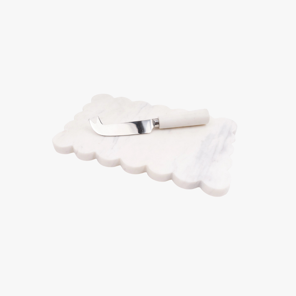 White scalloped cheese board with a cheese knife on a white background
