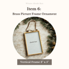 Brass picture frame ornament with 'abode box' text on a wooden surface with greenery.