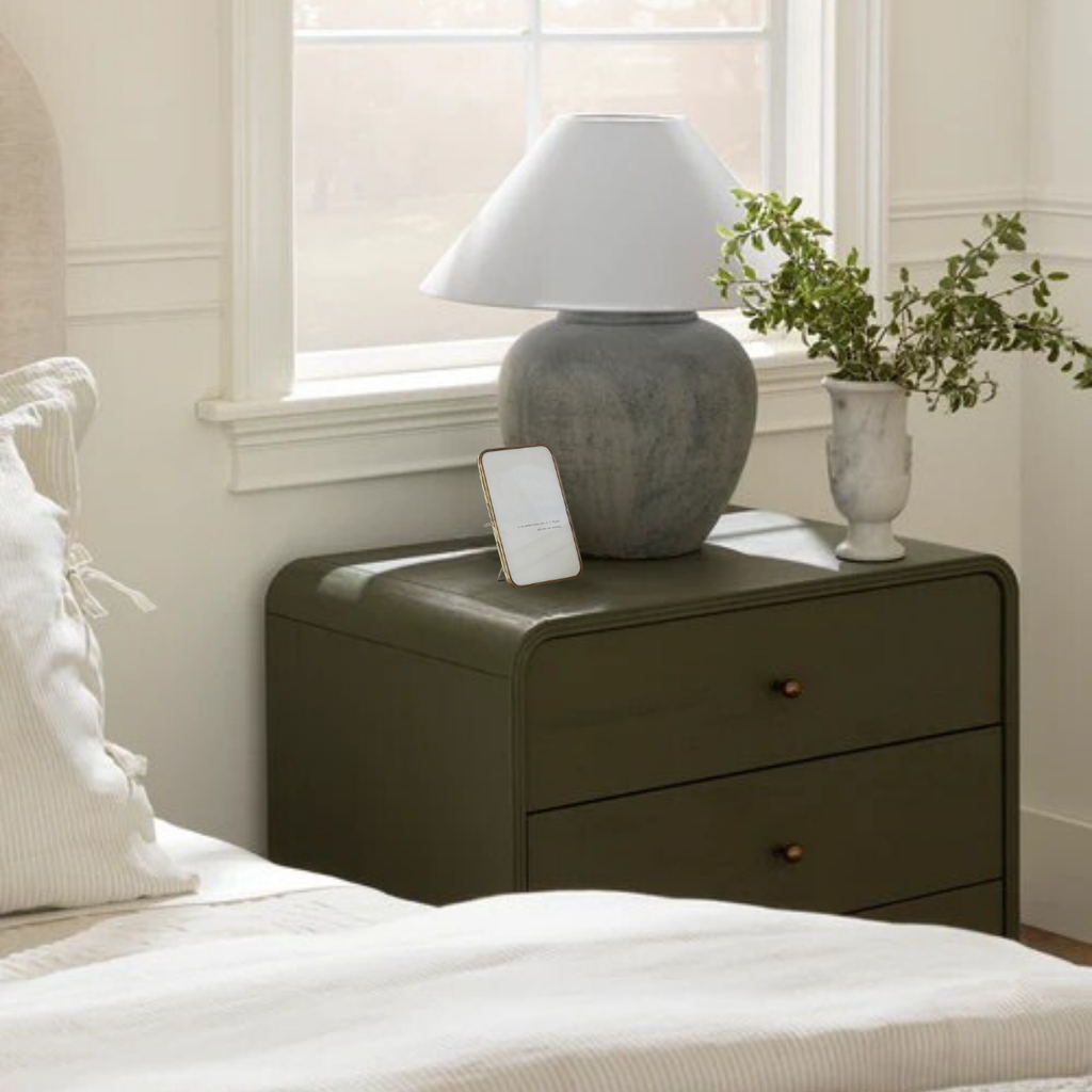 Green nightstand with brass picture frame, lamp and plant in a bedroom setting