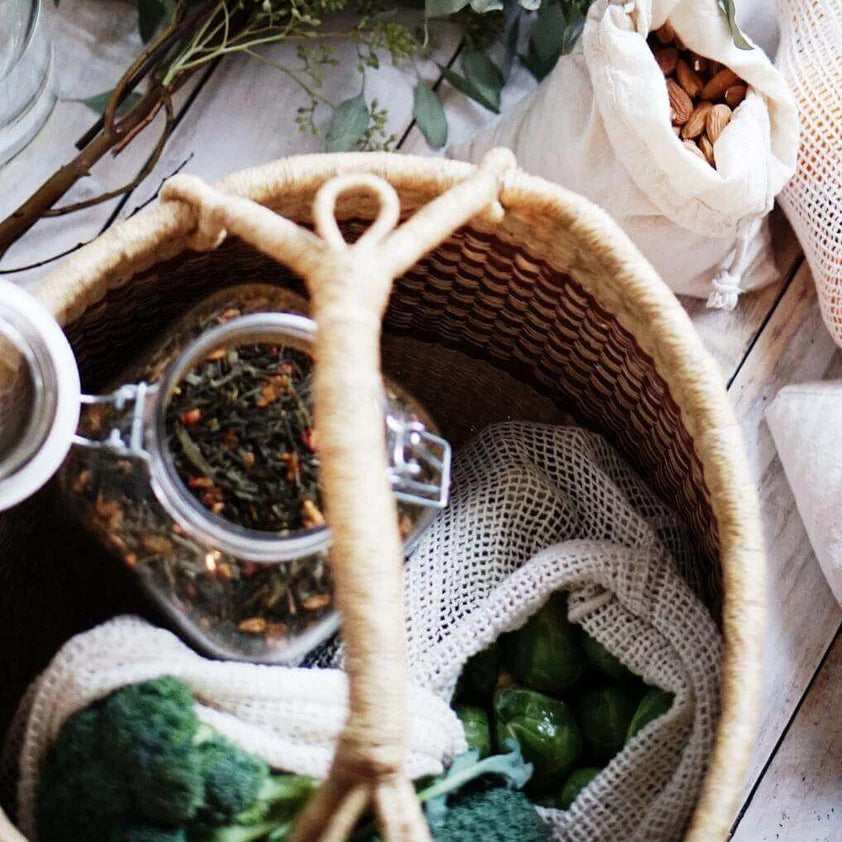 Bouquet of greenery, woven basket with tea leaves, and a bag of nuts on a wooden surface.