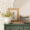 Decorative setting with a framed print of a dog, flowers in a vase, and a scalloped wood tray on a green cabinet.