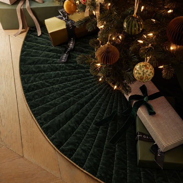 Velvet green christmas tree skirt with christmas gifts and decorated tree.