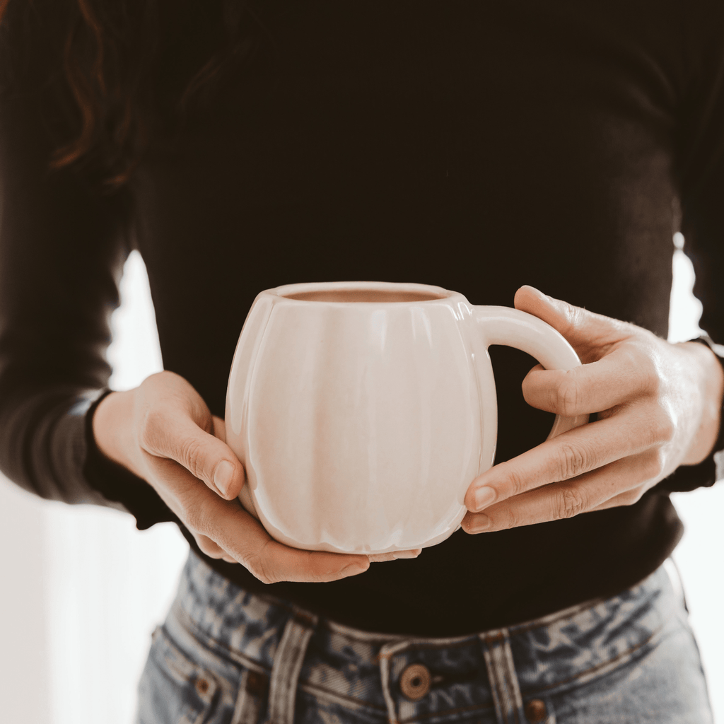 Person holding a white ceramic pumpkin mug with a blurred background