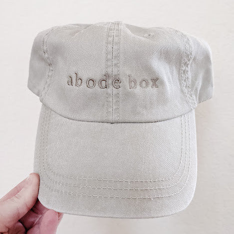A beige twill cap with the brand name 'Abode Box' embroidered on the front.