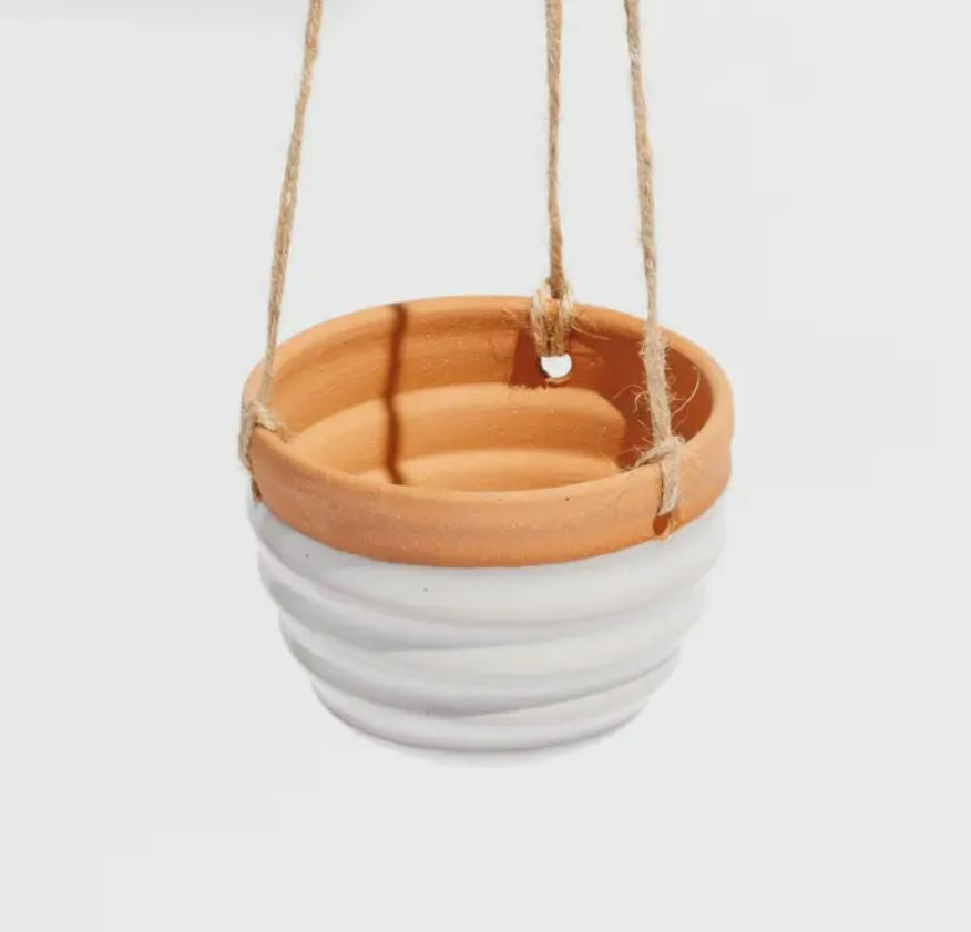 A small white hanging planter made of clay, with a terracotta-colored bottom and a white upper part, suspended by a jute twine.