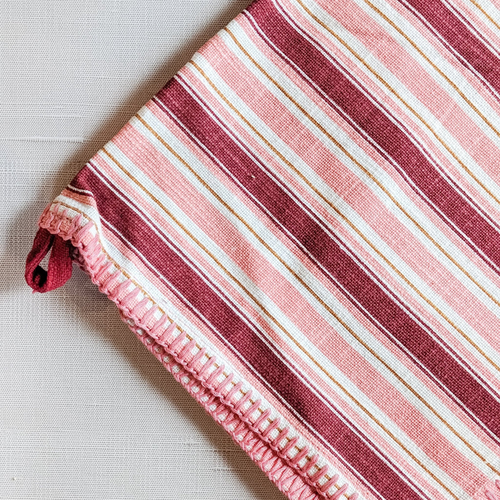 A red and pink striped holiday-themed kitchen tea towel laid out flat.